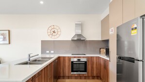 Una cocina moderna con un refrigerador de acero inoxidable, un horno Bosch, armarios de madera, un lavamanos de acero inoxidable y un reloj de pared.