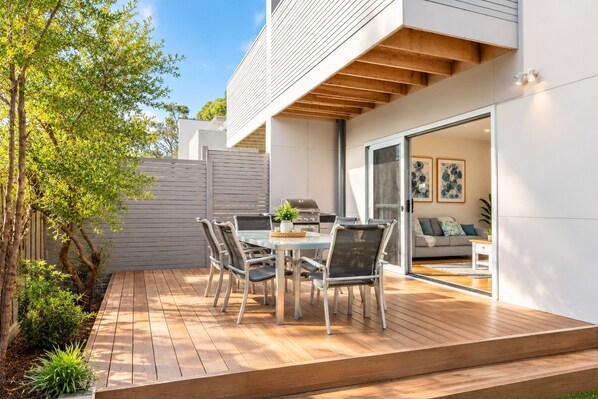 A modern outdoor patio with a dining table and chairs, a barbecue grill, and a view into the house through a glass door. - Unit 5 Broughton town house, beach walk only 20 meters!! (Cowes)