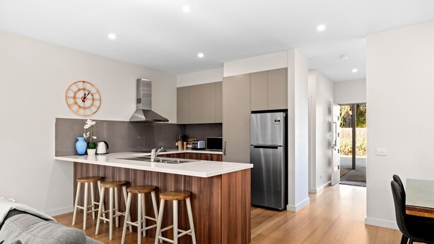 Une cuisine moderne dotée d’un îlot central, d’appareils électroménagers en acier inoxydable et de tabourets en bois.