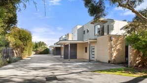 Un immeuble résidentiel moderne doté d’une allée couverte, d’un garage et d’un petit jardin à l’avant.