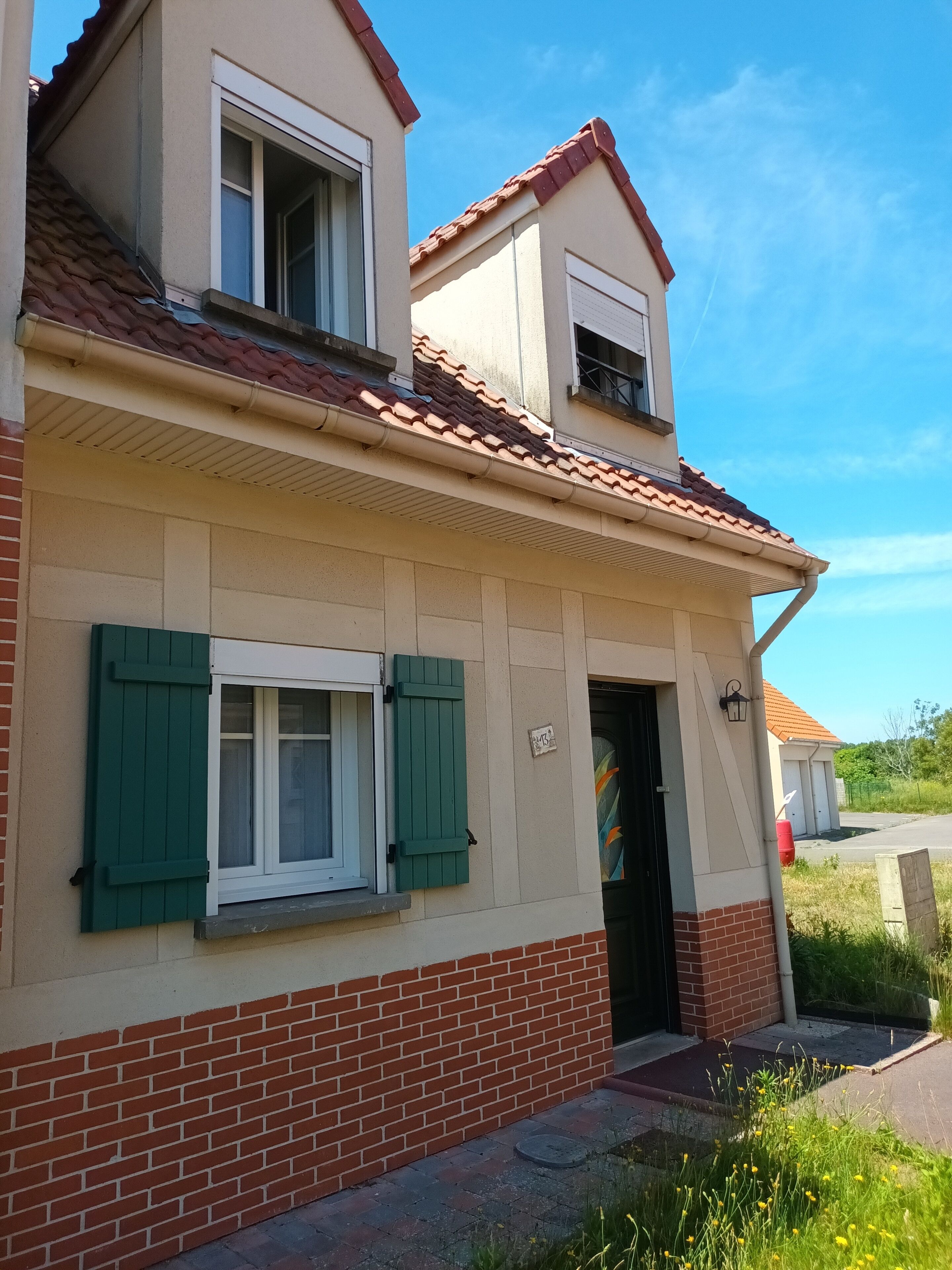A two-story house with a red-tiled roof, green shutters, and a brick base.