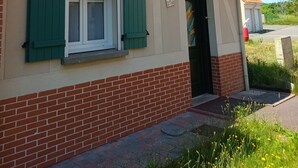 Ein zweistöckiges Haus mit rotem Ziegeldach, grünen Fensterläden und einer Ziegelbasis.