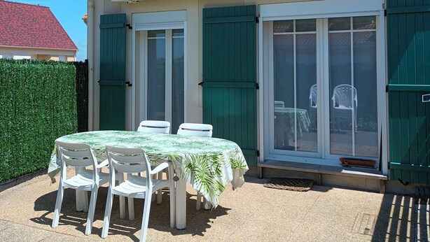 Ein Haus mit rotem Ziegeldach, einer überdachten Terrasse mit Tisch und Stühlen und einem grünen Zaun.