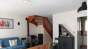 Ein modernes Wohnzimmer mit einem blauen Sofa, einer Holzbank, einem Esstisch und einer Treppe, die in einen Küchenbereich führt.