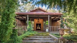 A wooden gazebo with a tiled roof, surrounded by lush greenery and stone steps leading to it.