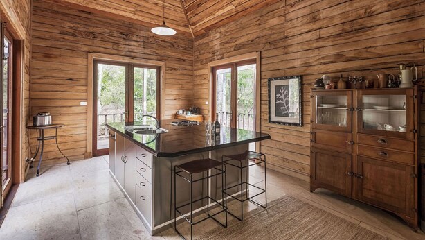 A wooden cabin kitchen with a central island, bar stools, and a cabinet with glass doors.