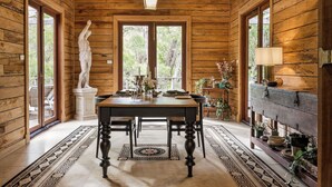 A wooden interior with a dining table, chairs, a statue, and a lamp.