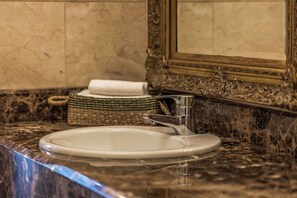 A bathroom with a marble sink, a gold-framed mirror, and a woven basket with a towel.