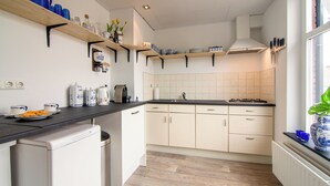A kitchen with wooden shelves, white cabinets, and a black countertop. - Vakantiewoning Vieverdwas (Yerseke)