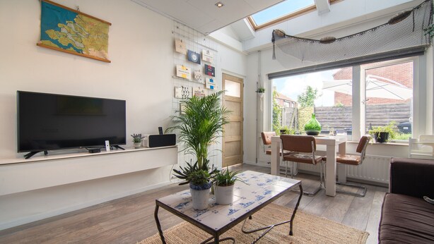 A modern living room with a flat-screen TV, a coffee table, and a sofa. There are potted plants on the coffee table and a large window providing natural light. - Vakantiewoning Vieverdwas (Yerseke)