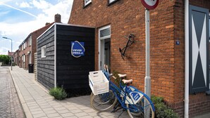 A blue delivery bike with a white basket parked next to a black building with a sign reading "VIEVER DWAS.nl". - Vakantiewoning Vieverdwas (Yerseke)