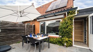 A patio with a table and chairs, a wooden fence, and a door leading to a covered area. - Vakantiewoning Vieverdwas (Yerseke)