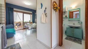 Una sala de estar moderna con comedor, una cocina con un ventanal grande y un baño con un mueble verde y un lavabo blanco.