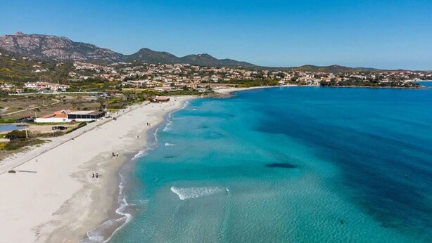 Un pueblo costero con playa, aguas azules cristalinas y montañas al fondo.