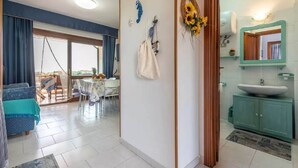 Una habitación con comedor, un baño con lavamanos y espejo, y vistas a través de un ventanal.
