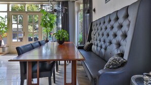 A dining area with a wooden table, black chairs, and a grey upholstered sofa with patterned cushions. - Characteristic House With Wellness in Augustinusga (Augustinusga)