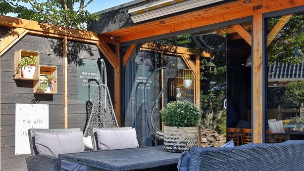 An outdoor seating area with wicker furniture and a hanging chair, a large potted plant, and a sign with text. - Characteristic House With Wellness in Augustinusga (Augustinusga)