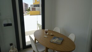 A modern dining area with a wooden table, white chairs, a glass of water, a book, and a starfish decoration. - Le Meilleur Appartement à Santa Margarita Immo365 (Roses)