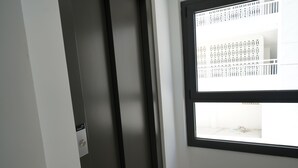 A room with a dark door, a window with a white grid pattern, and a visible light switch. - Le Meilleur Appartement à Santa Margarita Immo365 (Roses)