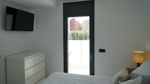 A bedroom with a bed, a dresser, a TV mounted on the wall, and a door leading to an outdoor area. - Le Meilleur Appartement à Santa Margarita Immo365 (Roses)
