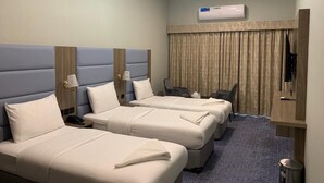 A hotel room with two beds, a desk, a chair, an air conditioning unit, and a curtain. - Silver Sand Hotel (Dubai)