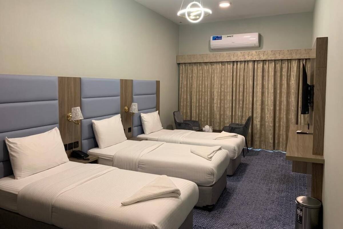 Ein Hotelzimmer mit zwei Betten, einem Schreibtisch, einem Sessel, einer Klimaanlage und einem Vorhang.