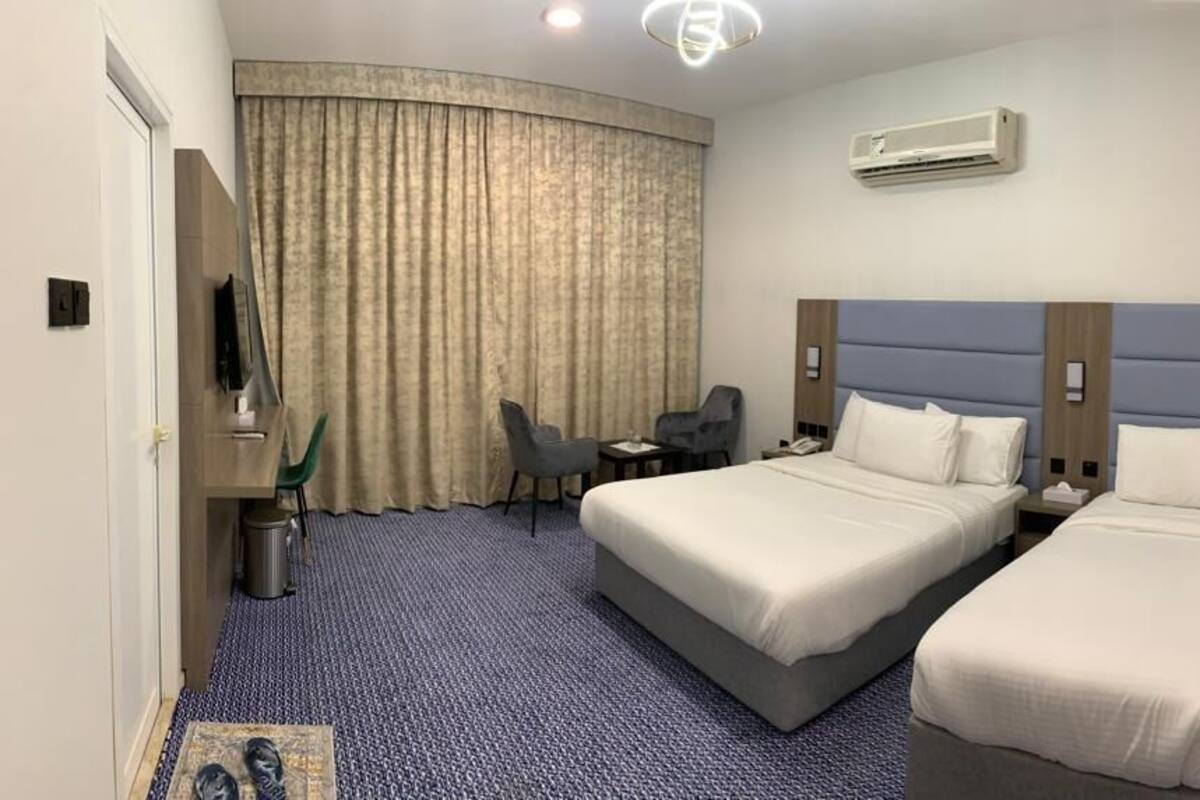 Ein Hotelzimmer mit zwei Betten, einem Schreibtisch, einem Stuhl und einem großen Fenster mit Vorhängen.