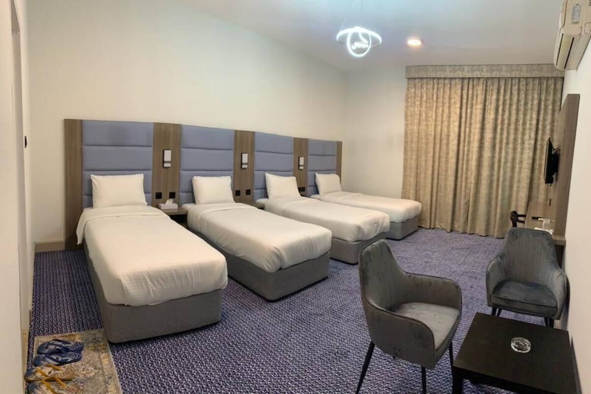 Ein Hotelzimmer mit drei Einzelbetten, einer kleinen Sitzecke inklusive zwei Stühlen und einem Tisch.