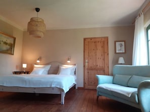 A bedroom with a bed, bedside tables, a hanging light fixture, a wooden door, a blue sofa, and a painting on the wall. - Holiday Home Landlust (Mirow)