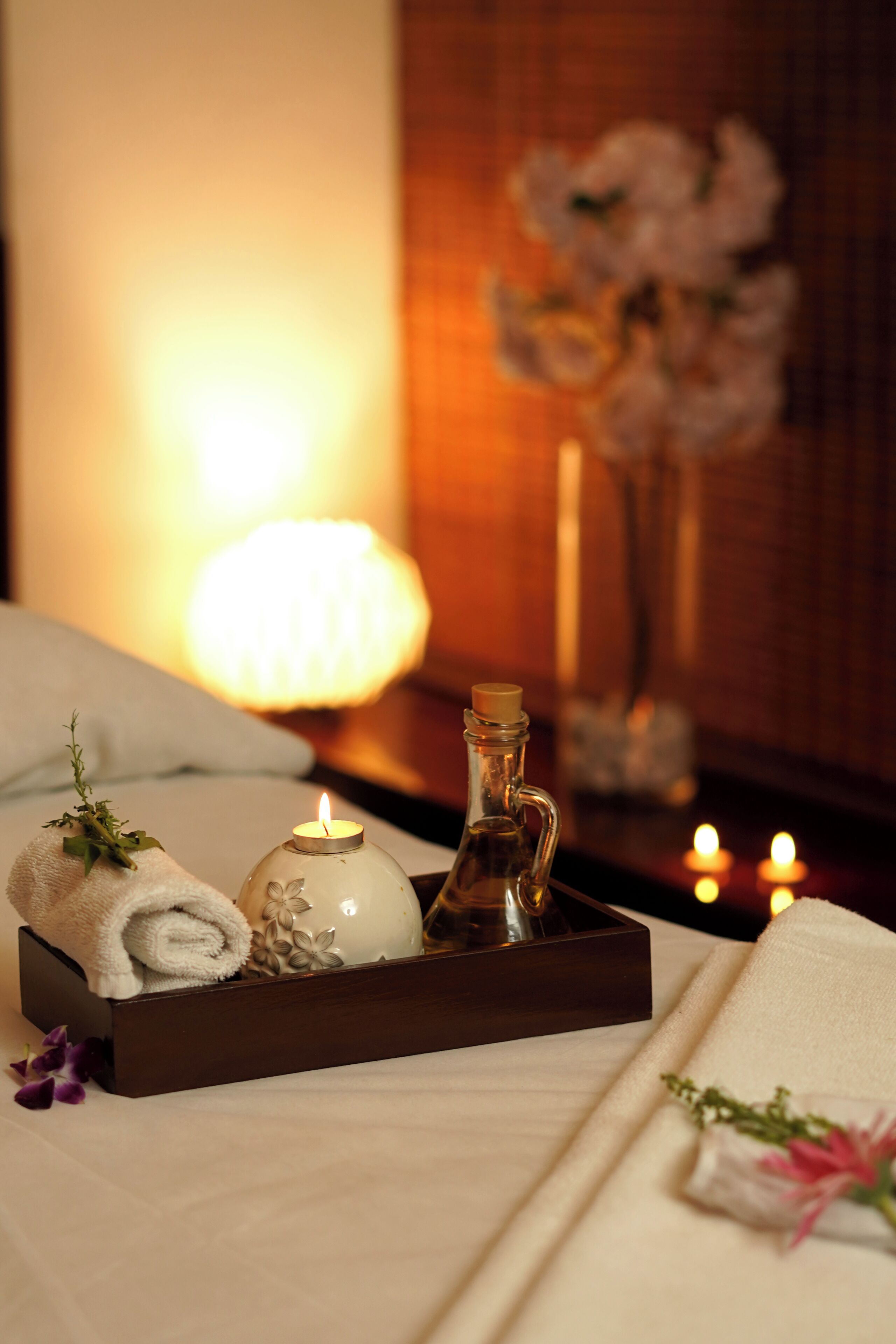 A neatly arranged tray with a rolled towel, a decorative vase, and a candle on a bed.