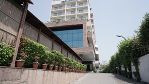 A hotel with a modern glass facade and a traditional wooden structure on the left. - ALCOR HOTEL JAMSHEDPUR (Golmuri)