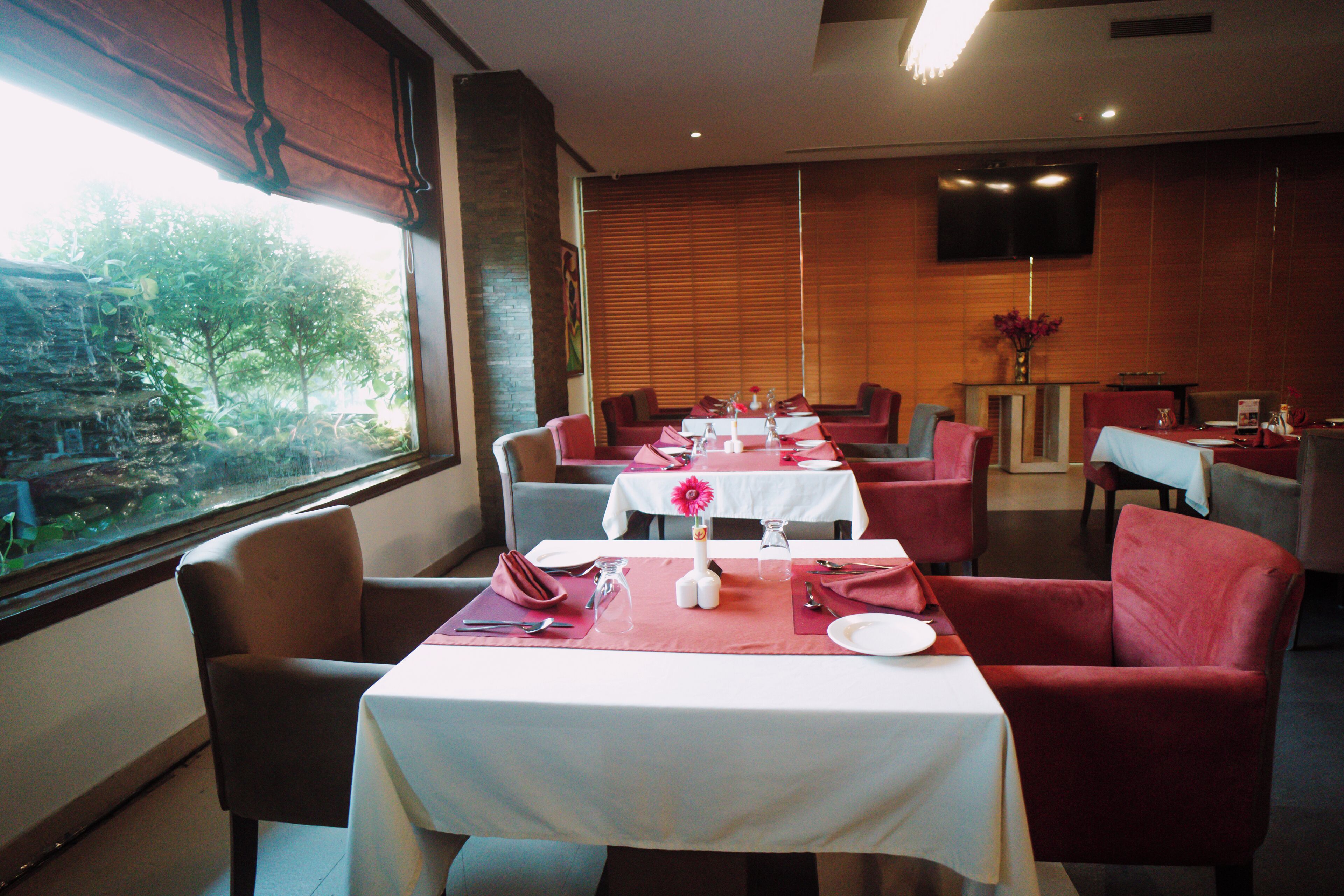 A restaurant with tables set for dining, chairs, and a view of greenery outside.