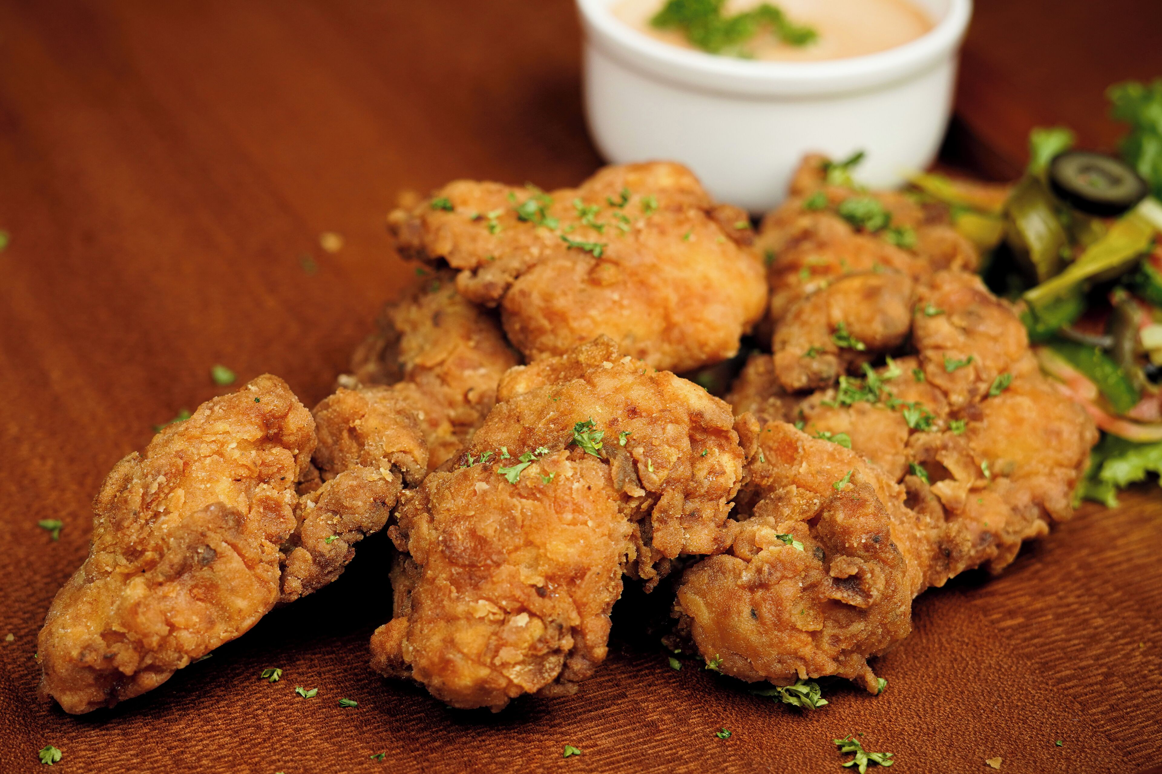 Un montón de trozos de pollo frito decorados con hierbas, acompañados de un recipiente pequeño con salsa.