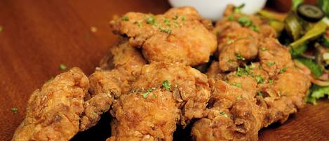 Un montón de trozos de pollo frito decorados con hierbas, acompañados de un recipiente pequeño con salsa.