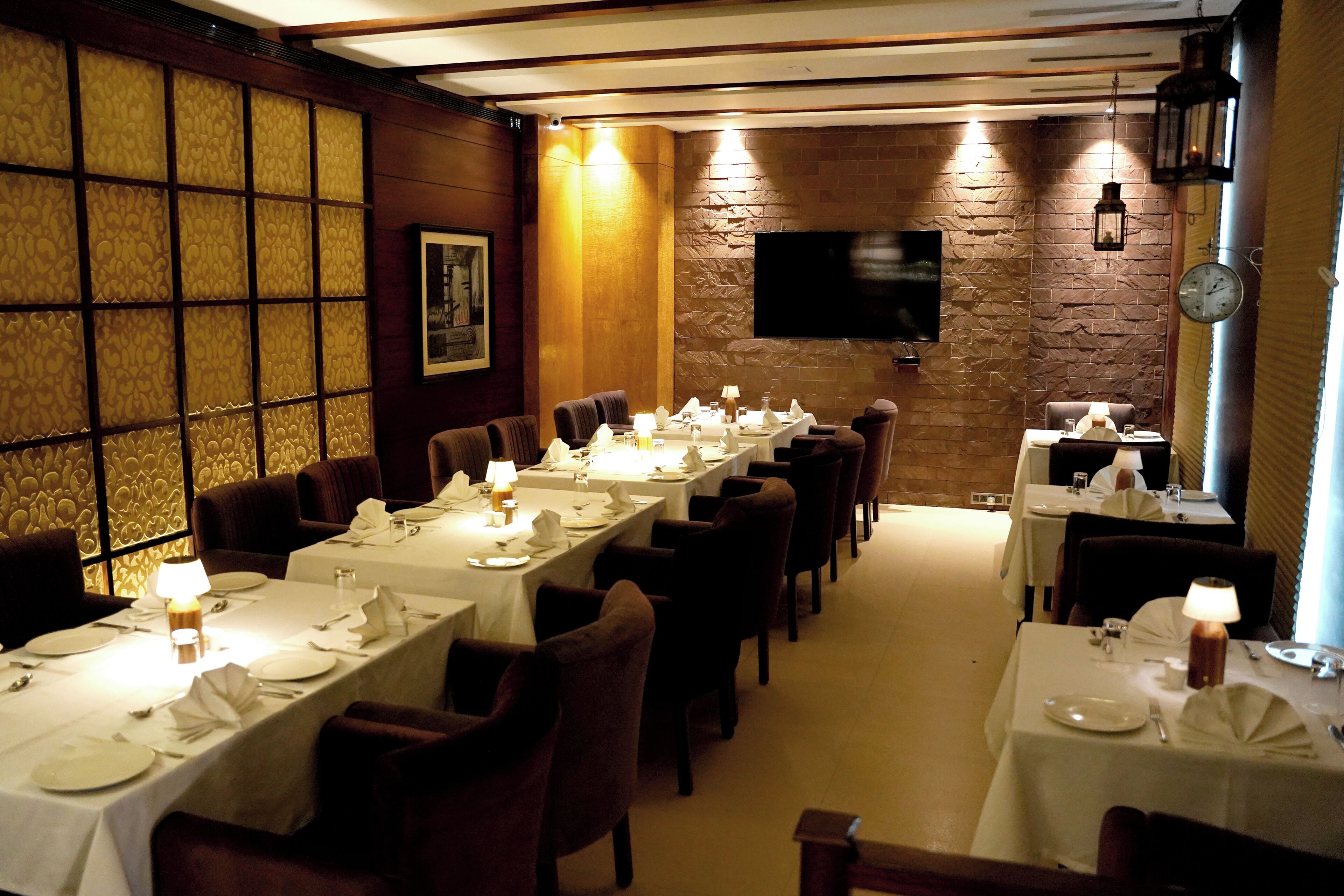 Een restaurant met lange tafels klaar voor het dineren, een bakstenen muur en een flatscreen televisie aan de muur.