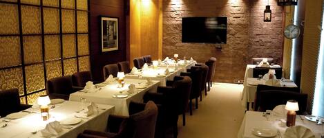 Een restaurant met lange tafels klaar voor het dineren, een bakstenen muur en een flatscreen televisie aan de muur.