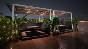 An outdoor patio area with a covered seating area, potted plants, and a well-lit ambiance. - ALCOR HOTEL JAMSHEDPUR (Golmuri)