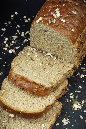 Une miche de pain recouverte de graines, entourée de graines éparpillées.