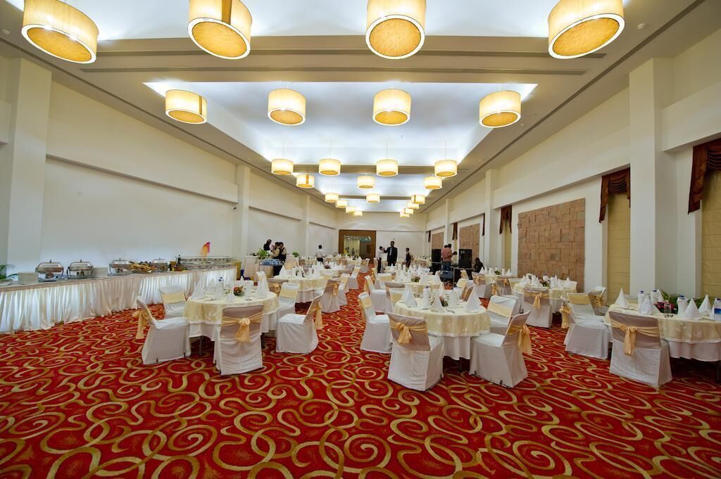 A banquet hall with round tables set for a formal event, featuring a red carpet and white tablecloths.