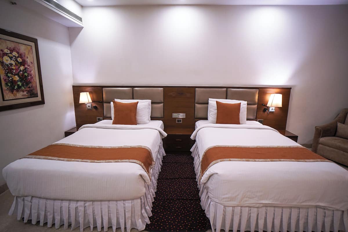 Habitación de hotel con dos camas, cada una con cabecera, lámparas de noche y una manta marrón.