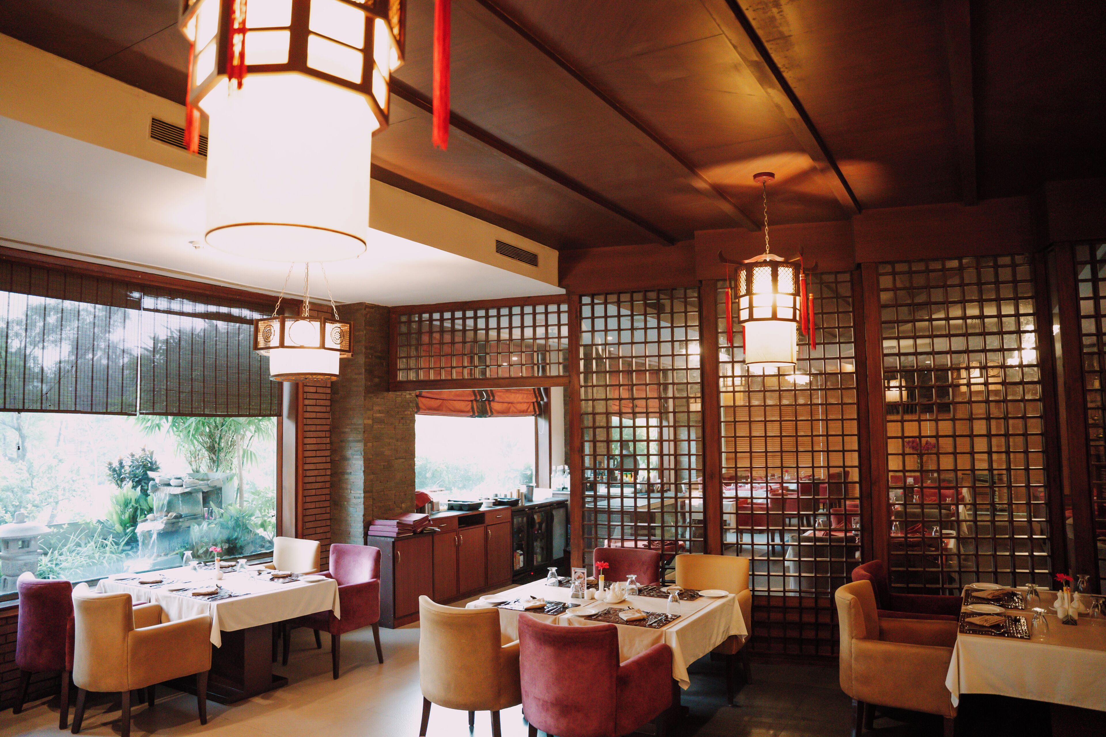 A restaurant with tables set for dining, wooden beams on the ceiling, and a view through a window.