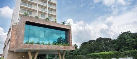A modern hotel with a glass facade, a flat roof, and a sign reading "The Alcor Hotel".