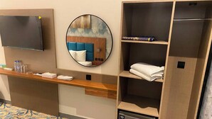 A hotel room with a flat-screen TV, a round mirror, a wooden shelf with towels, a small refrigerator, and a patterned carpet. - Tamarind Hotel (Dubai)