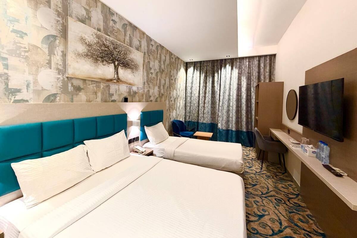 A hotel room with a large bed, a desk, a chair, a television, and a painting on the wall.