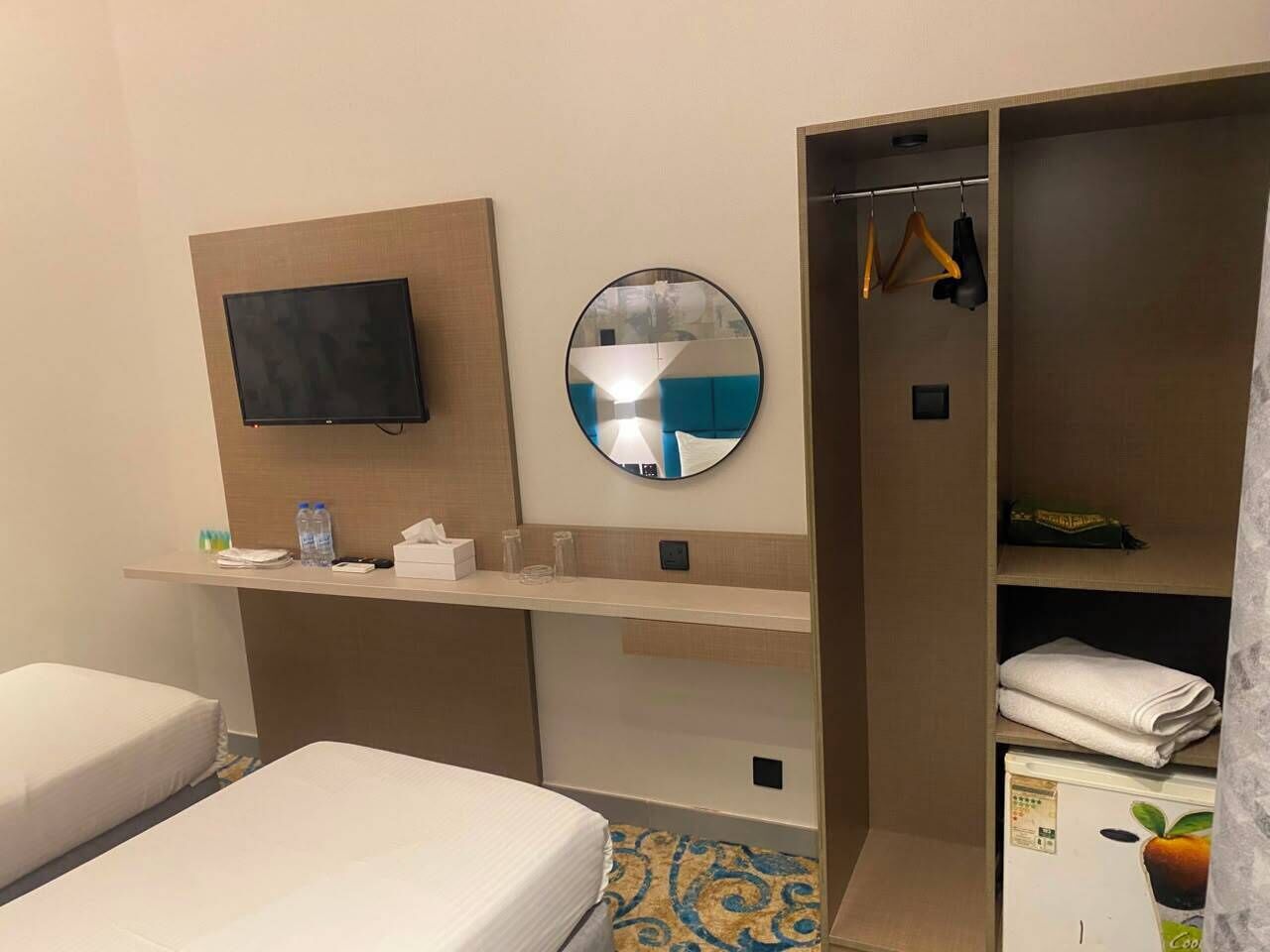 Une chambre d’hôtel avec deux lits, une télévision, un miroir, une armoire et une petite table avec des articles de toilette.