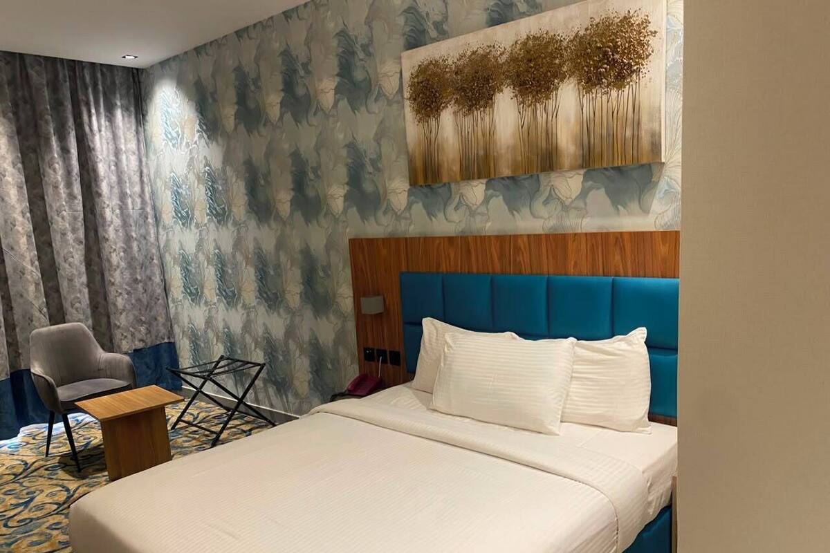 A hotel room with a large bed, a chair, a small table, and a painting on the wall.