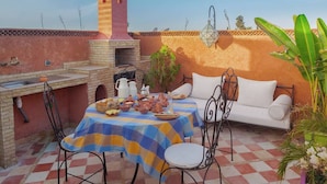Terrassa exterior amb un paviment de pissos, una taula preparada amb plats, un sofà blanc i un petit forn de rajola.