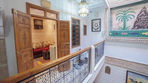 Una escala amb barana ornamentada, una porta de fusta amb detalls esculpits i una paret amb obra emmarcada i una làmpada decorativa al sostre.