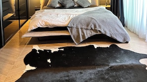 A modern bedroom with a bed, a geometric wall art piece, and a fur rug.