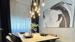 A modern dining area with a rectangular table, black chairs, a hanging light fixture, and a large abstract painting on the wall.